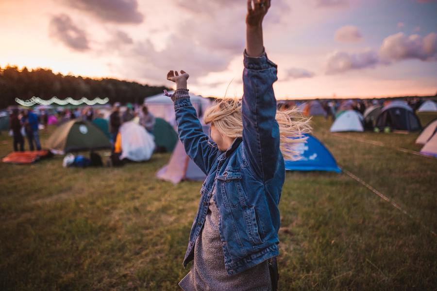 Woman with arms thrown up in the air at sunset in a festival campsite
