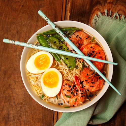 prawn ramen bowl with egg, pees, sesame seeds, and blue chopsticks