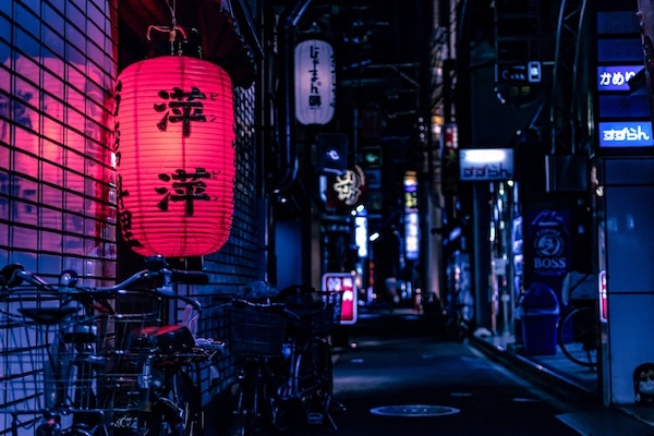 glowing red Japanese lantern stands out against dimly lit blue street with bicycles and shop signs