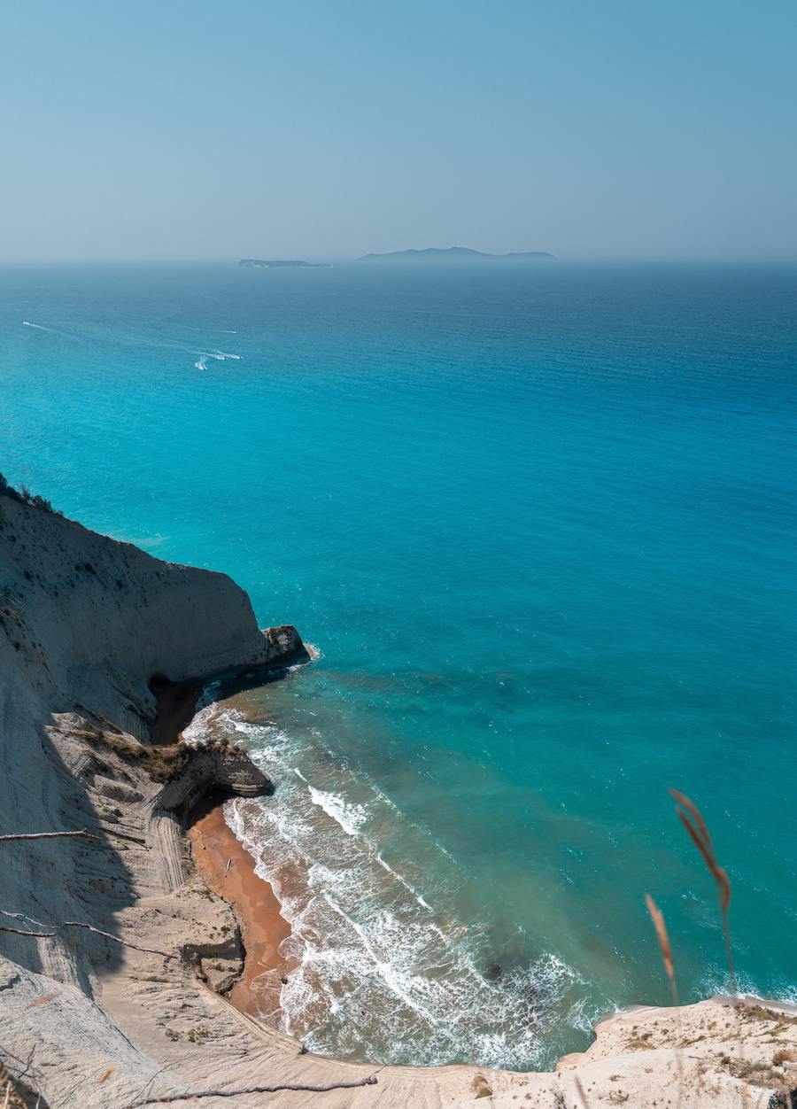 arial shot from cliff-top of island beach with deep, vibrant blue waters